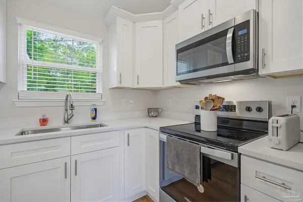 a kitchen with stainless steel appliances granite countertop a sink dishwasher a microwave stove and white cabinets with wooden floor