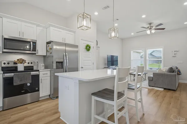 a kitchen with stainless steel appliances kitchen island granite countertop a refrigerator a stove top oven a dining table and chairs with wooden floor