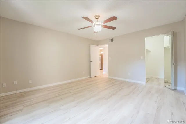 a view of an empty room with wooden floor and a ceiling fan
