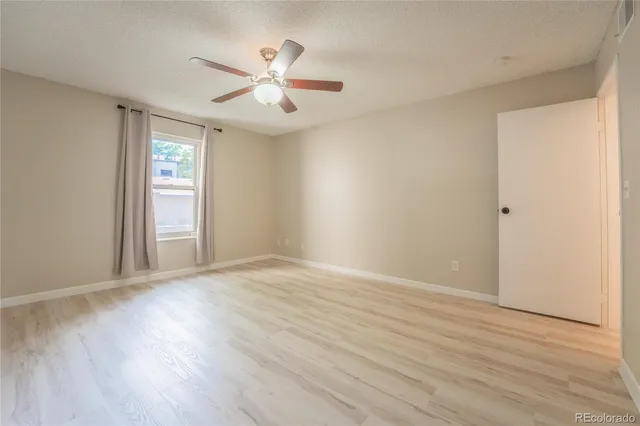 an empty room with wooden floor chandelier fan and windows