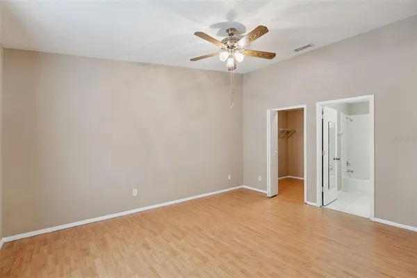 an empty room with a chandelier fan and wooden floor
