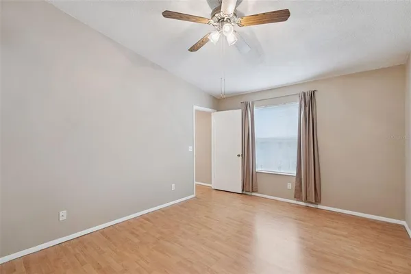 a view of an empty room with wooden floor and a ceiling fan