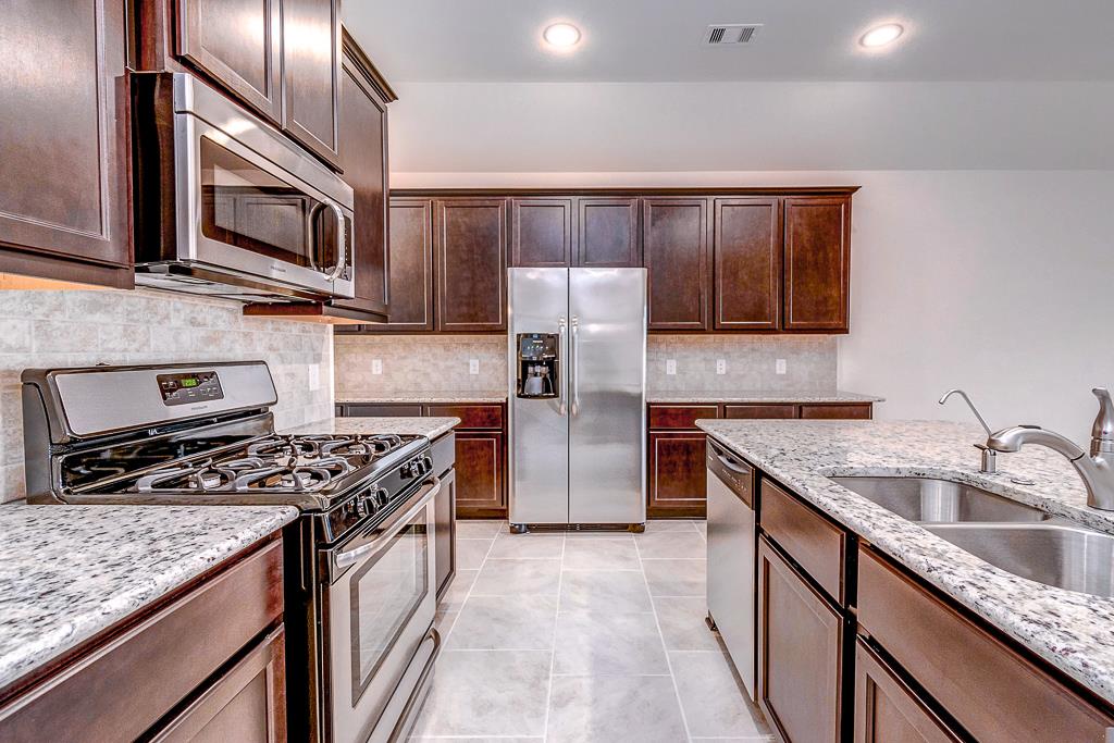 24314 North Newcastle Bay Trail Spring, TX 77389 - Photo 10 of 32 a kitchen with stainless steel appliances granite countertop a stove top oven a sink dishwasher a refrigerator and a microwave oven with wooden floor
