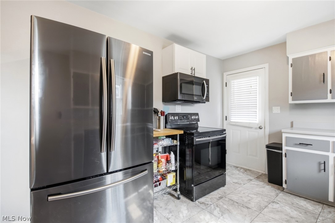 12684 Taylor Wells Road Chardon, OH 44024 - Photo 26 of 40 Stainless steel refrigerator, black microwave, black range, white upper cabinetry, and gray and white lower cabinetry