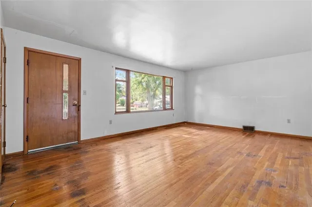 an empty room with wooden floor fan and windows