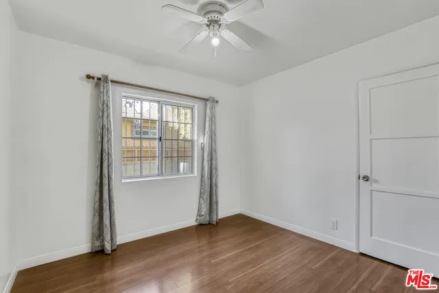 an empty room with wooden floor chandelier fan and windows