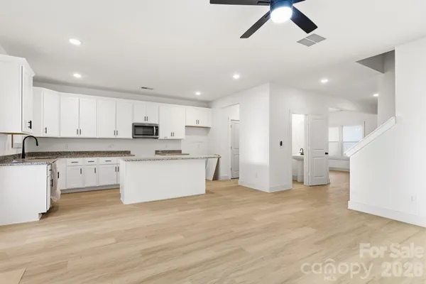 a large kitchen with stainless steel appliances kitchen island granite countertop a stove a sink a refrigerator and white cabinets with wooden floor