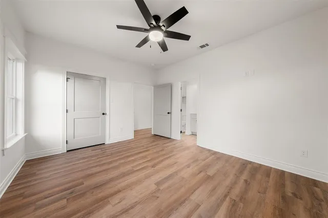 an empty room with wooden floor fan and windows