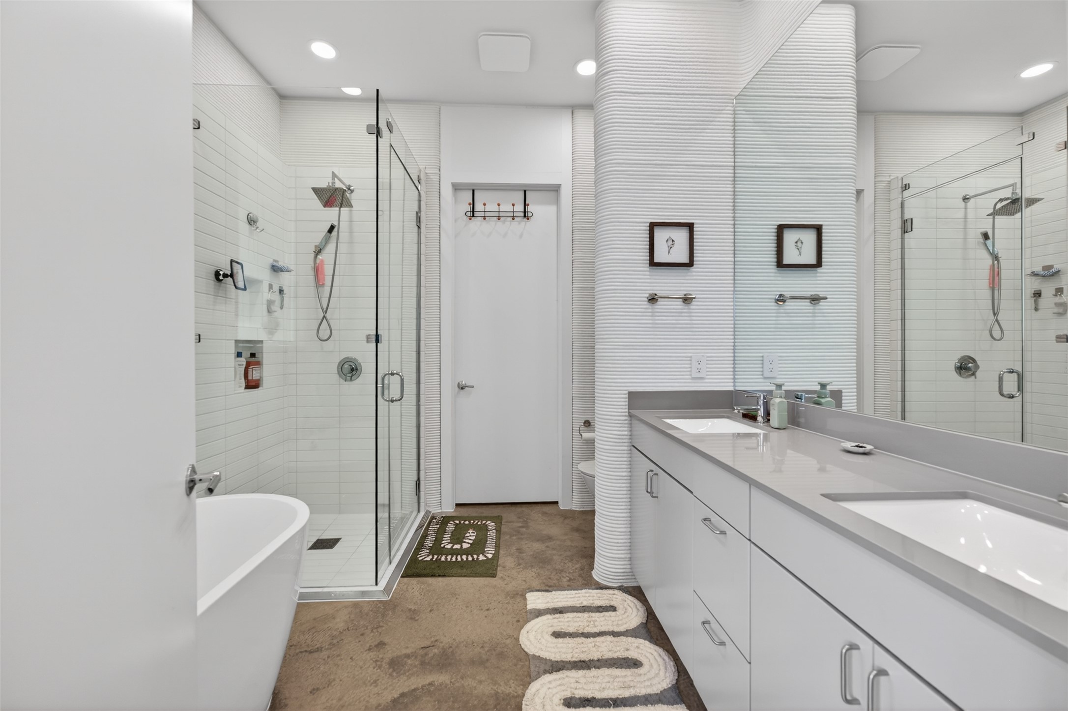 308 Painted Sunset Drive Georgetown, TX 78628 - Photo 24 of 26 Bathroom featuring a dual vanity with light gray countertops and undermount sinks, a freestanding soaking tub, a glass-enclosed shower with subway tile surround, textured white accent wall, and concrete-finish flooring