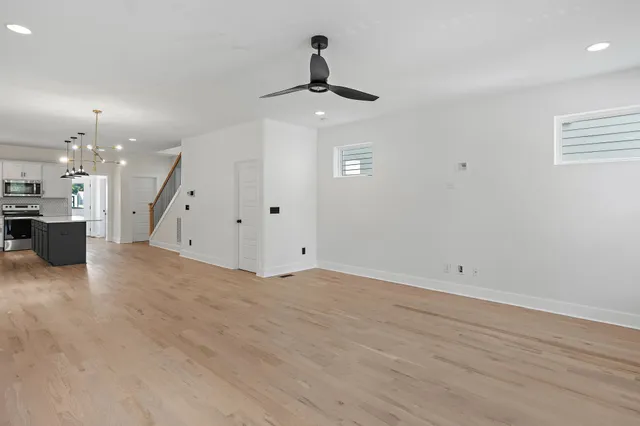 an empty room with wooden floor ceiling fan and kitchen view