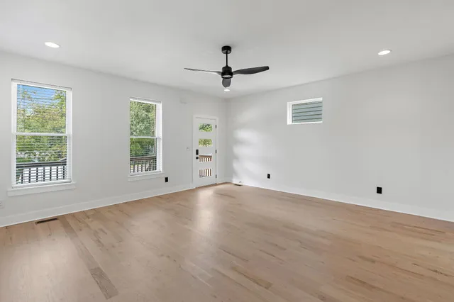 an empty room with wooden floor ceiling fan and windows