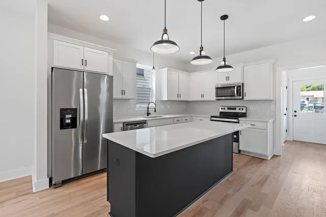 a kitchen with kitchen island granite countertop a sink a center island a refrigerator and a wooden floor