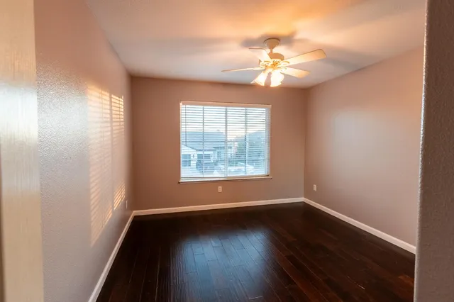 an empty room with wooden floor fan and windows