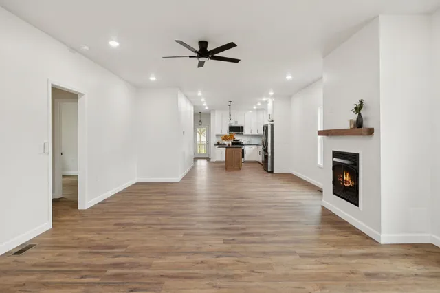 an empty room with wooden floor a ceiling fan white walls and windows