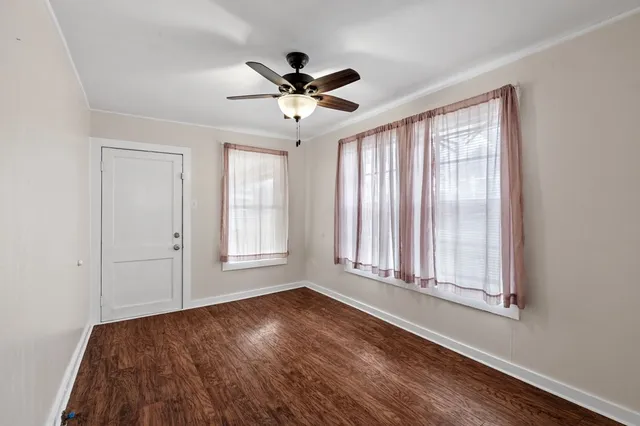 an empty room with wooden floor fan and windows