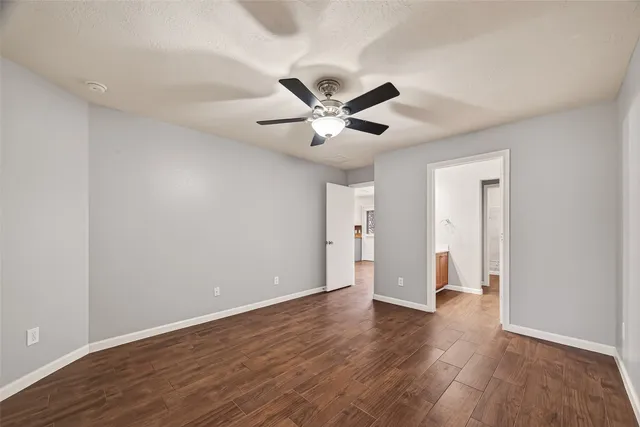 a view of an empty room with wooden floor and a ceiling fan