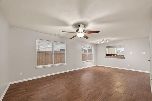 a view of an empty room with chandelier fan and wooden floor
