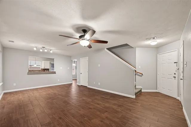 a view of an empty room with wooden floor and a ceiling fan
