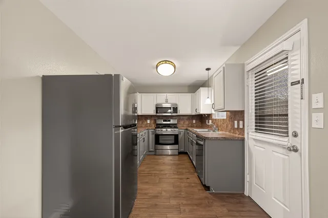 a kitchen with stainless steel appliances granite countertop a refrigerator a sink dishwasher a stove with white cabinets and wooden floor