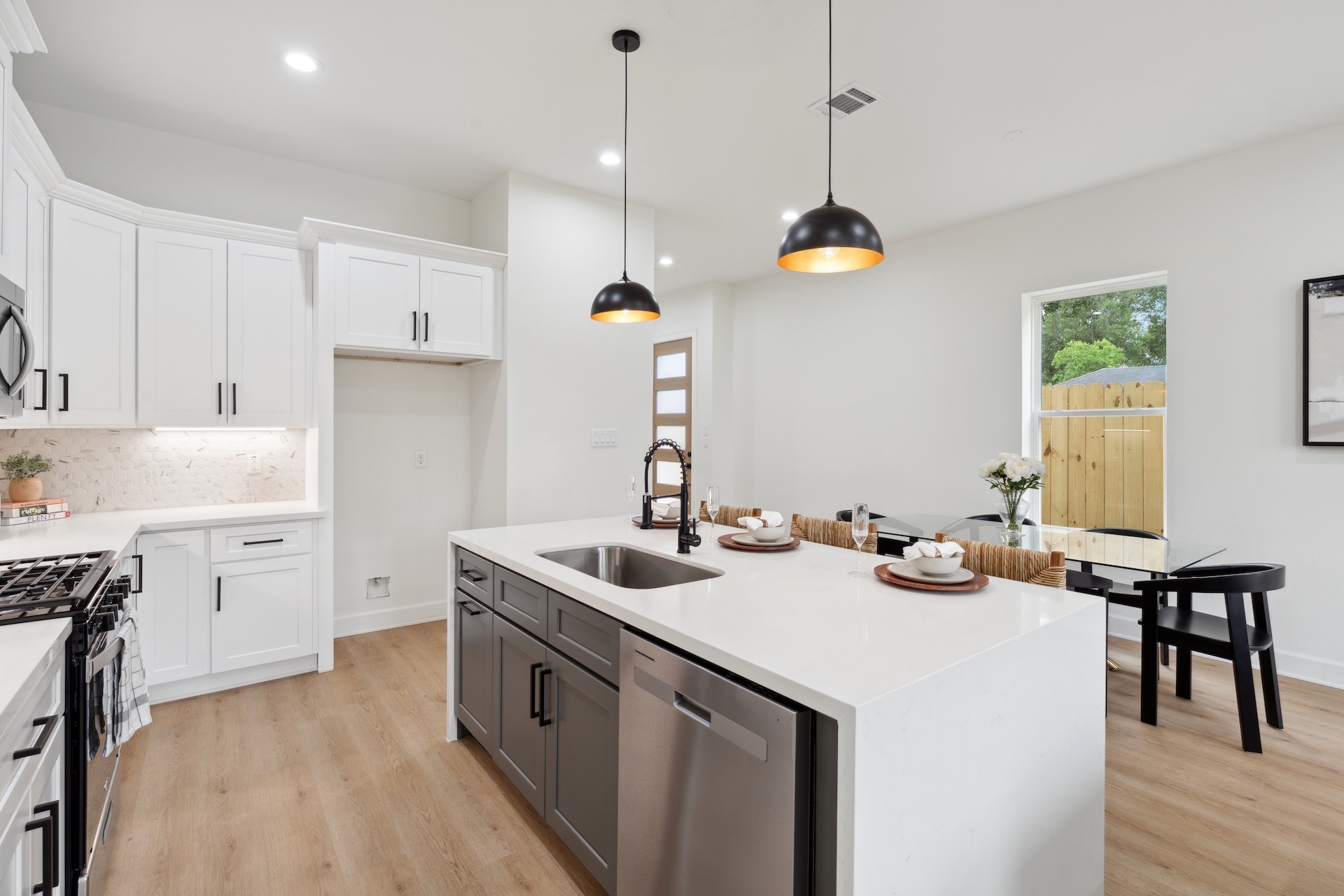 Thoughtfully designed kitchen hub — quartz waterfall island, built-in dishwasher, gas cooktop wall, and an adjacent refrigerator alcove with overhead storage.