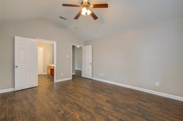a view of an empty room with wooden floor and a ceiling fan