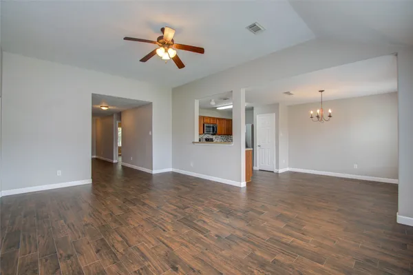 a view of an empty room with wooden floor and a ceiling fan