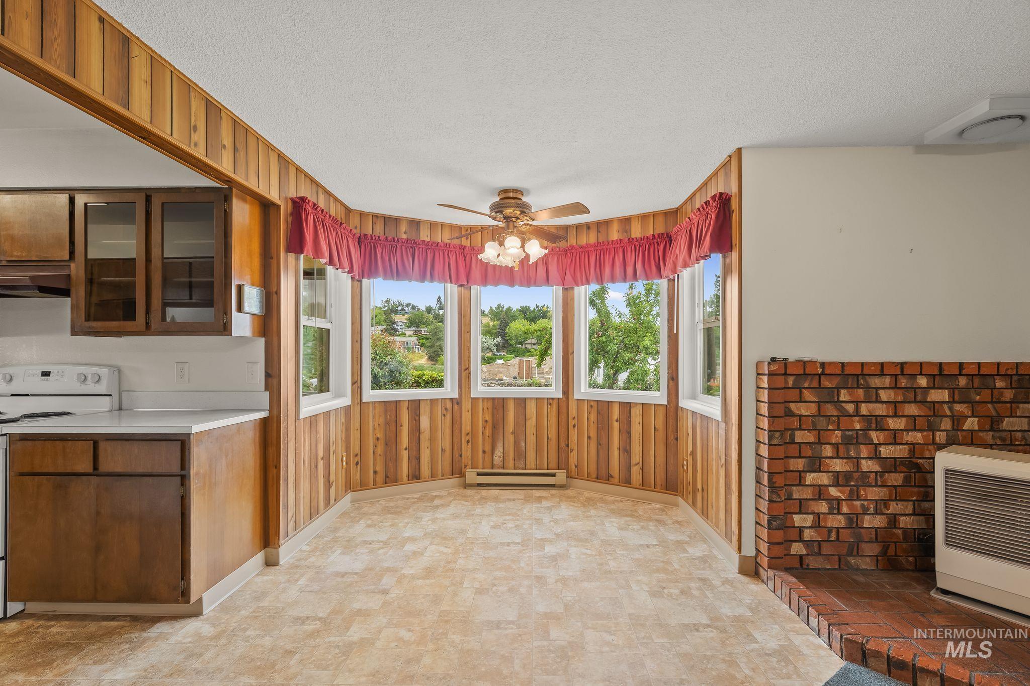 1721 3rd Street Lewiston, ID 83501 - Photo 9 of 45 Spacious living area featuring a brick fireplace, bay window, wood-finish wall paneling, and a ceiling fan