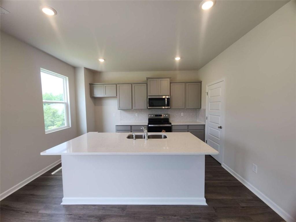 146 Aster Avenue Locust Grove, GA 30248 - Photo 3 of 28 a large kitchen with kitchen island a sink wooden floor and white cabinets