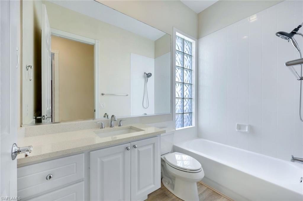 3108 Dominica Way Naples, FL 34119 - Photo 19 of 39 Bathroom featuring a white vanity with a light-colored countertop and integrated sink, a large wall-mounted mirror, a bathtub with a shower fixture, a toilet, and a glass block window