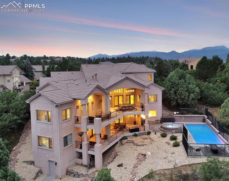 5039 Stonehill Road Colorado Springs, CO 80918 - Photo 3 of 50 Back of property at dusk featuring a balcony, a tiled roof, fence, a mountain view, and stucco siding