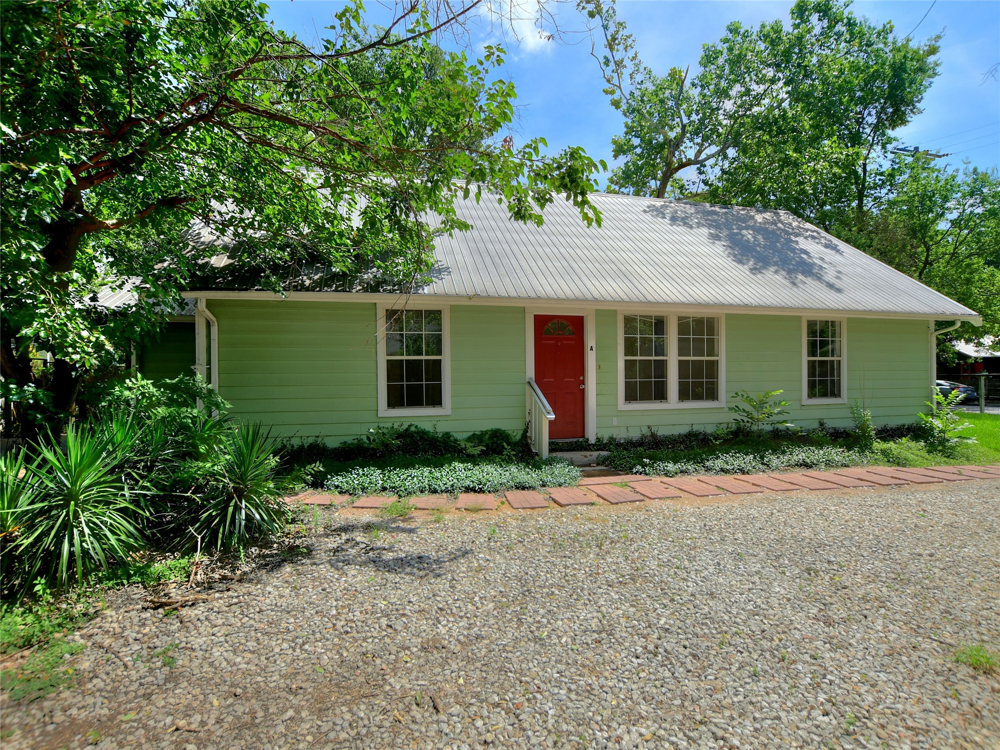 Light green exterior with a corrugated metal roof, featuring a vibrant red entry door