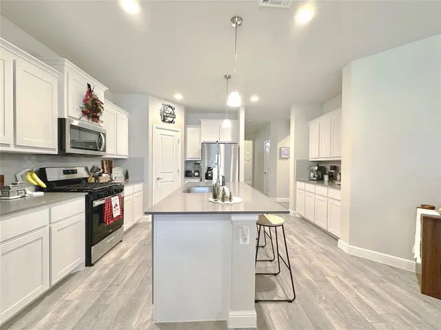 a kitchen with stainless steel appliances kitchen island granite countertop a stove a sink a refrigerator a microwave oven with white cabinets and wooden floor