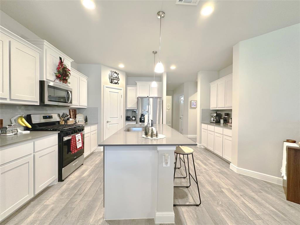 a kitchen with stainless steel appliances kitchen island granite countertop a stove a sink a refrigerator a microwave oven with white cabinets and wooden floor