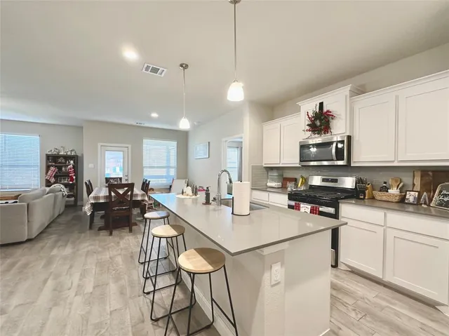a living room with stainless steel appliances kitchen island granite countertop a stove a sink a refrigerator and white cabinets with wooden floor