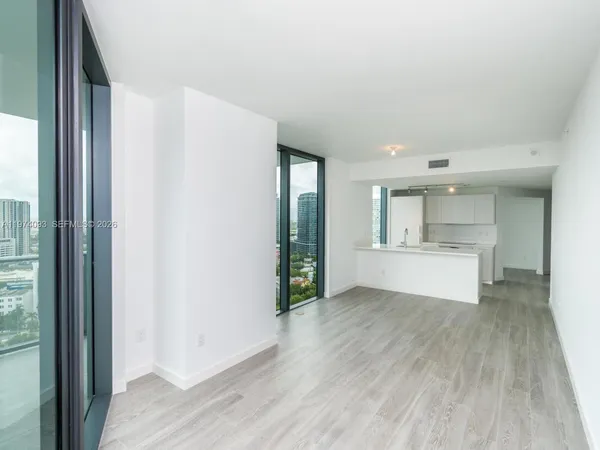 a view of an empty room with kitchen and a window