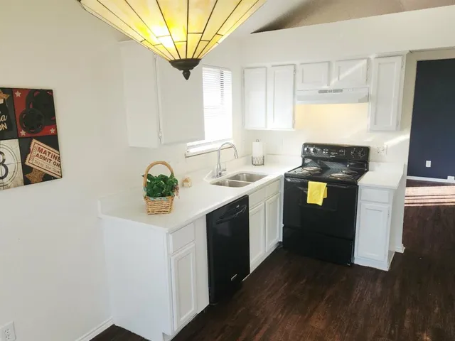 a kitchen with stainless steel appliances granite countertop a sink a stove a refrigerator white cabinets and wooden floor