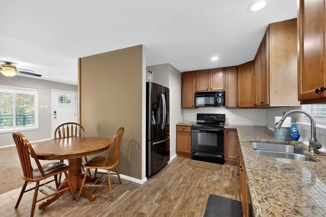 a kitchen with granite countertop stainless steel appliances a stove a refrigerator a sink dishwasher a dining table and chairs with wooden floor