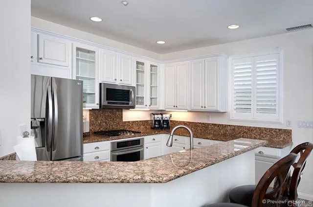a kitchen with granite countertop a sink stainless steel appliances and white cabinets