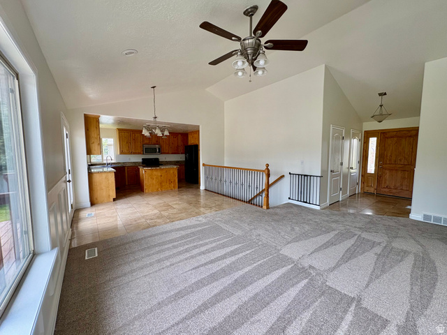 665 West State Road Lehi, UT 84043 - Photo 3 of 30 Vaulted great room with a ceiling fan, a kitchen featuring wood cabinetry and an island, a wood-finish front door with an adjacent window, and a carpeted main floor