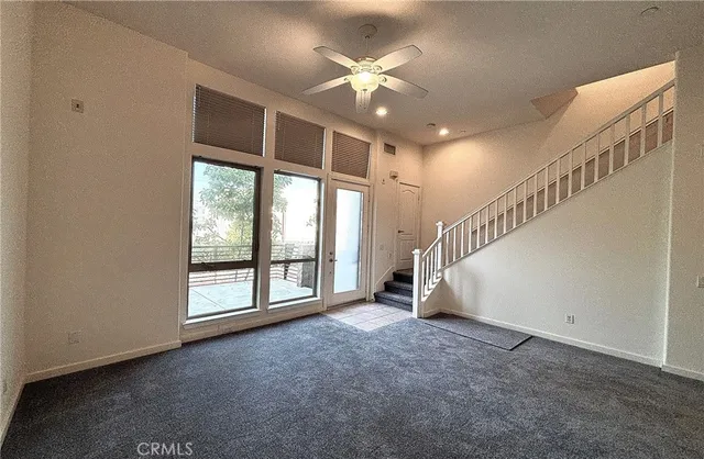 a view of an empty room with stairs and a ceiling fan