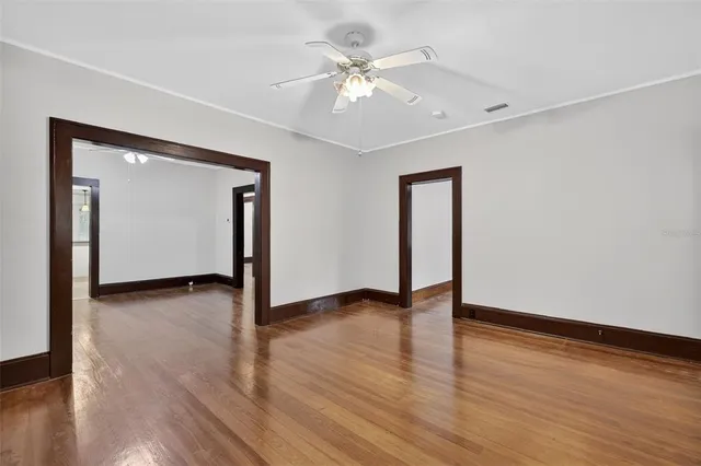 an empty room with wooden floor chandelier fan and windows