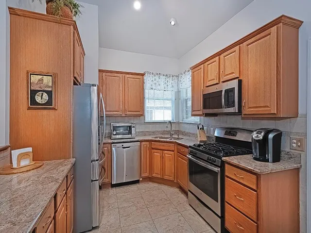 a kitchen with stainless steel appliances granite countertop a stove top oven a sink dishwasher and a refrigerator with wooden cabinets