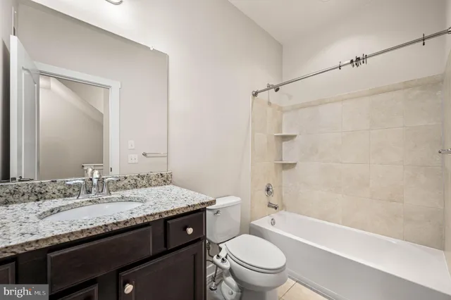 a bathroom with a granite countertop bathtub sink vanity mirror and toilet