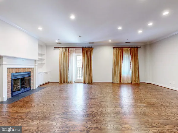 an empty room with wooden floor fireplace and windows