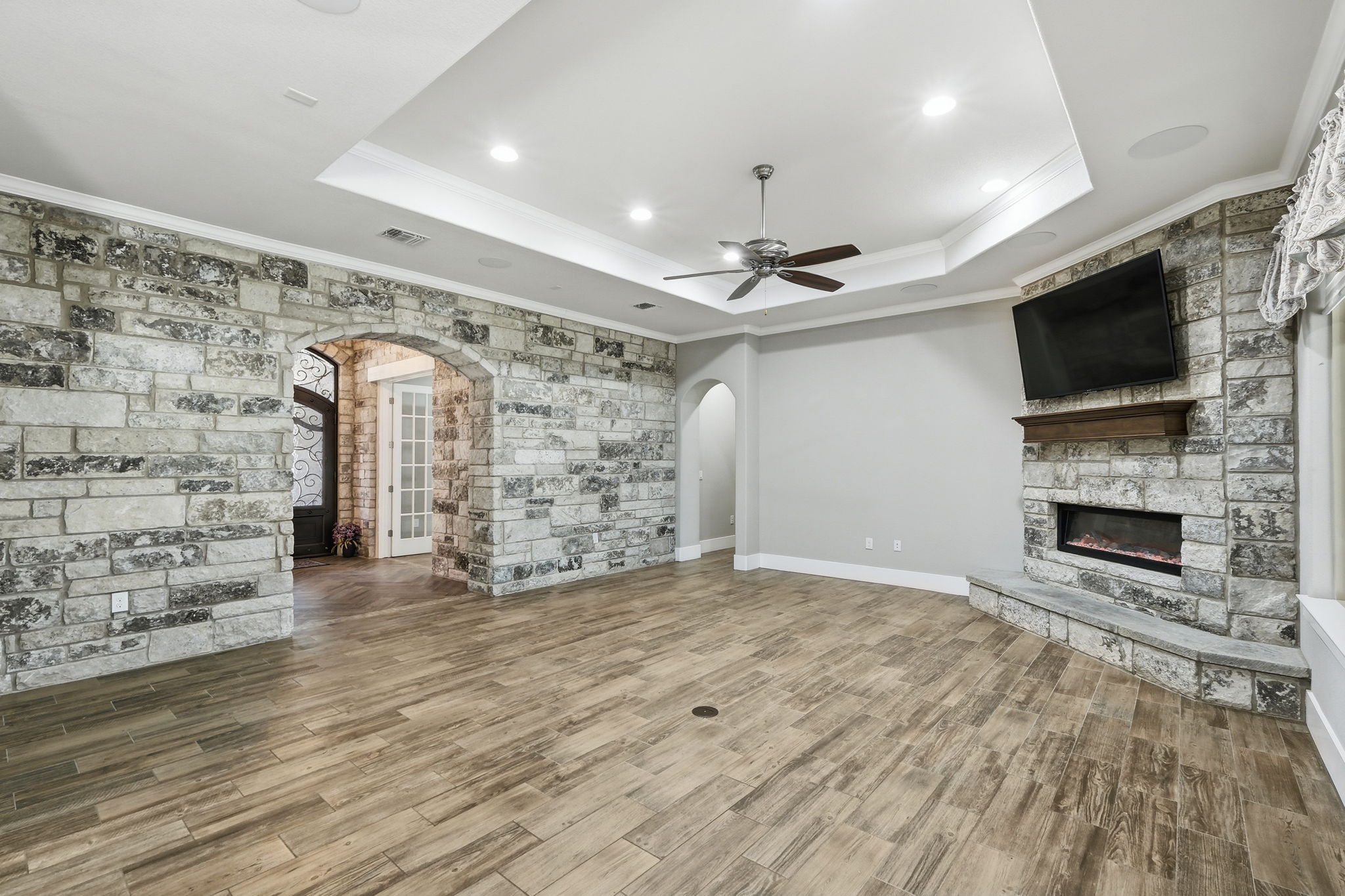 403 Highland Spring Lane Georgetown, TX 78633 - Photo 8 of 40 Unfurnished living room featuring ornamental molding, a stone fireplace, arched walkways, wood finished floors, and a ceiling fan