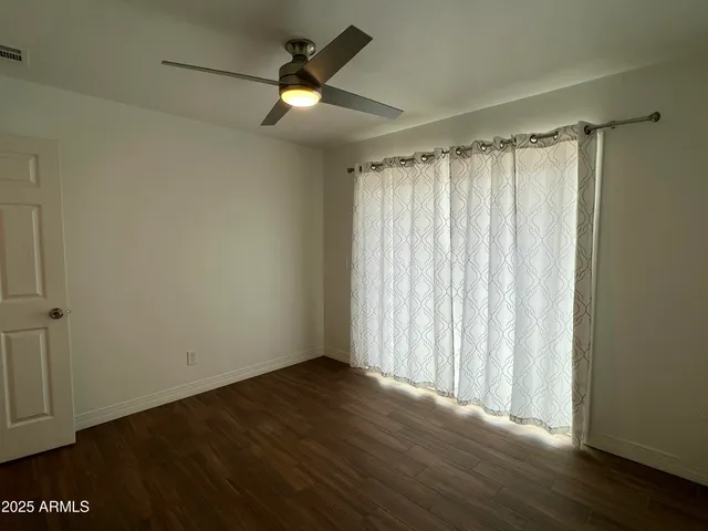 an empty room with wooden floor fan and windows