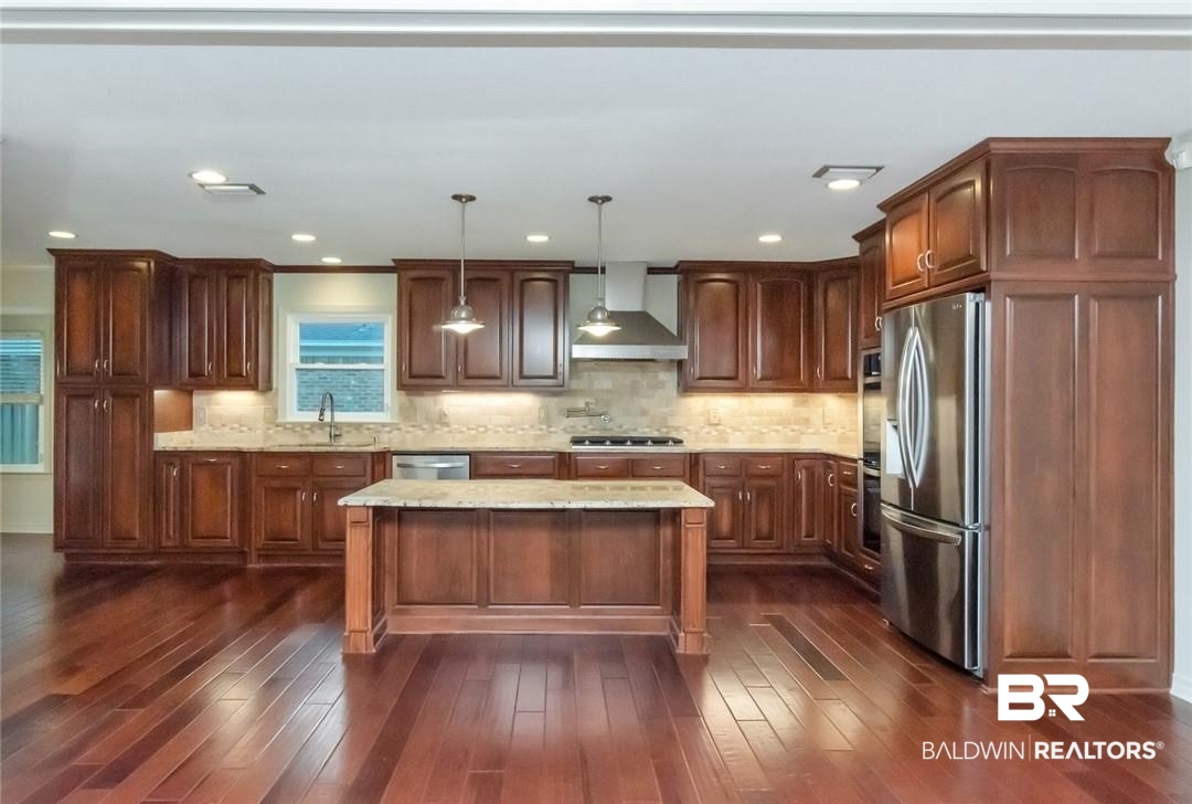 6109 Timberly Road North Mobile, AL 36609 - Photo 3 of 26 Kitchen featuring wall chimney exhaust hood, appliances with stainless steel finishes, hanging light fixtures, and dark wood-type flooring