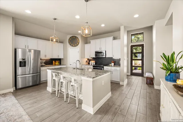 a kitchen with stainless steel appliances granite countertop a refrigerator a stove top oven a sink dishwasher and white cabinets with wooden floor