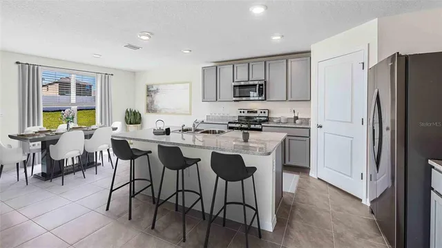 a kitchen with stainless steel appliances a dining table chairs refrigerator and sink