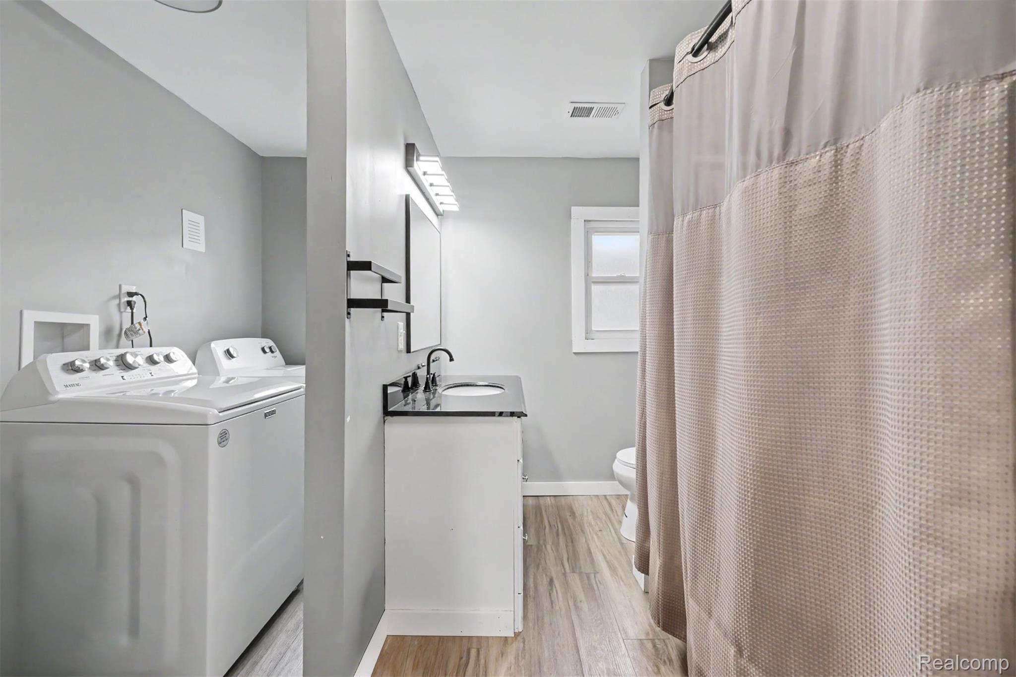 8397 Lane Street Detroit, MI 48209 - Photo 29 of 41 Full-sized laundry appliances, vanity with a black countertop and integrated sink, wall-mounted faucet, and wood-finish flooring